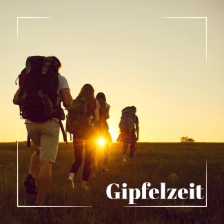Eine Gruppe junger Menschen wandert mit Rucksäcken bei Sonnenuntergang über einen Hügel